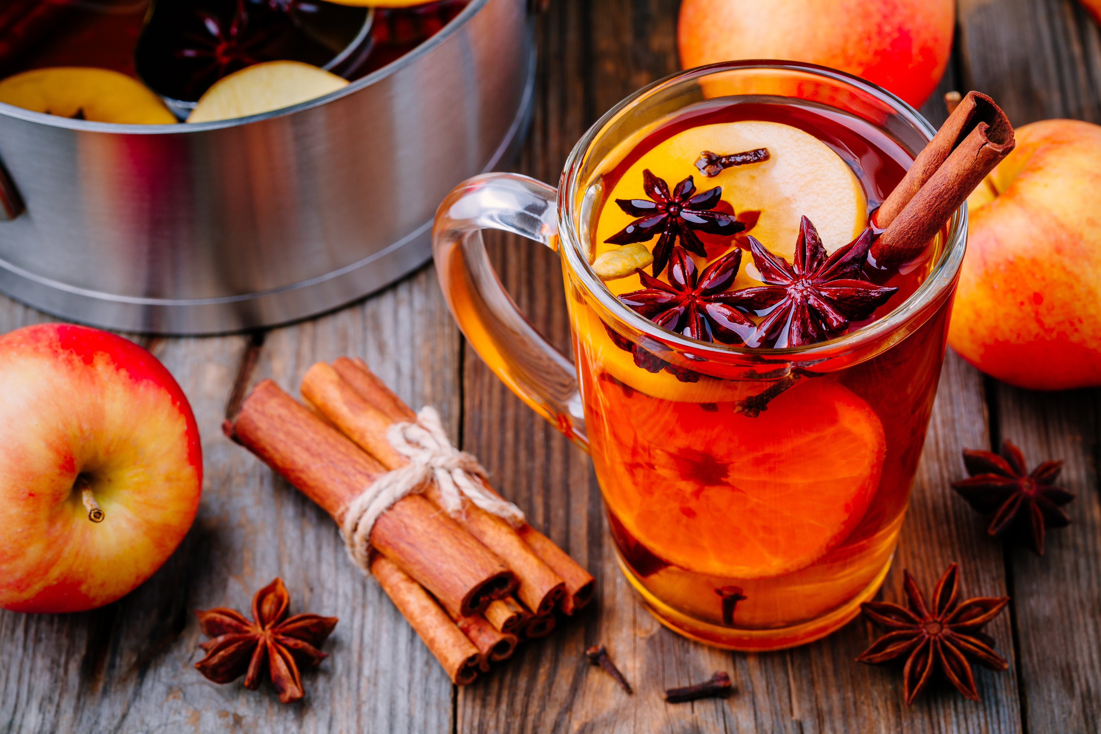  Hot mulled apple cider with cinnamon sticks, cloves and anise on wooden background